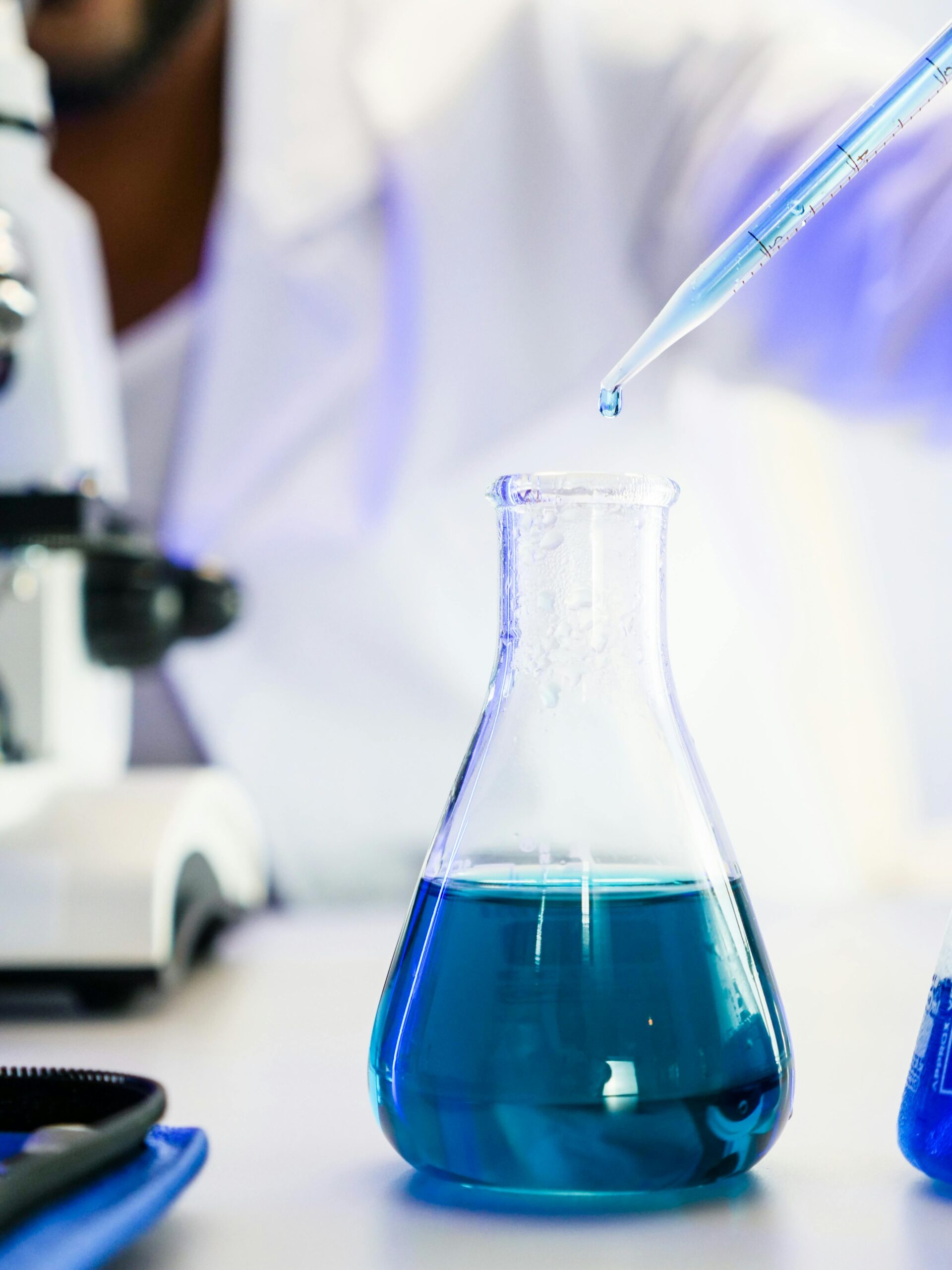 Close-up of blue liquid in Erlenmeyer flask with pipette in a modern lab setting.